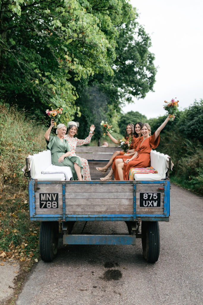 Bridal party wave to photographer and videographer as they leave for the wedding in Devon Rustic farm family wedding