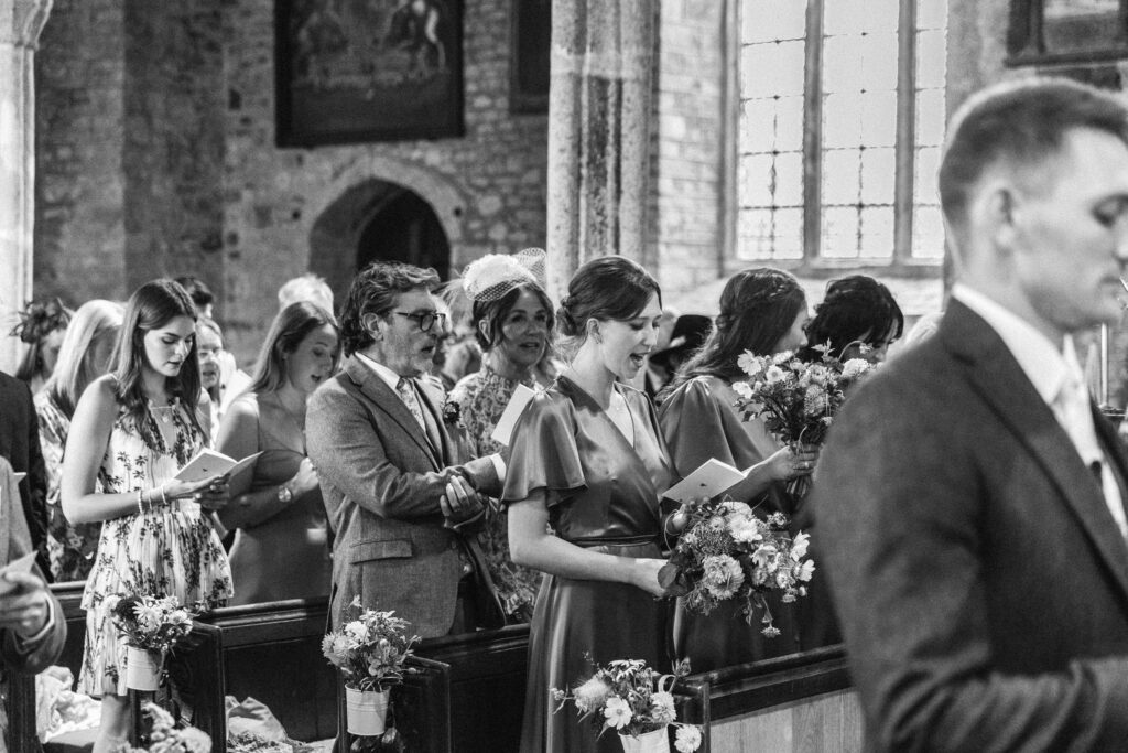guests singing hymns inside the church as bride walks down the isle in Devon wedding