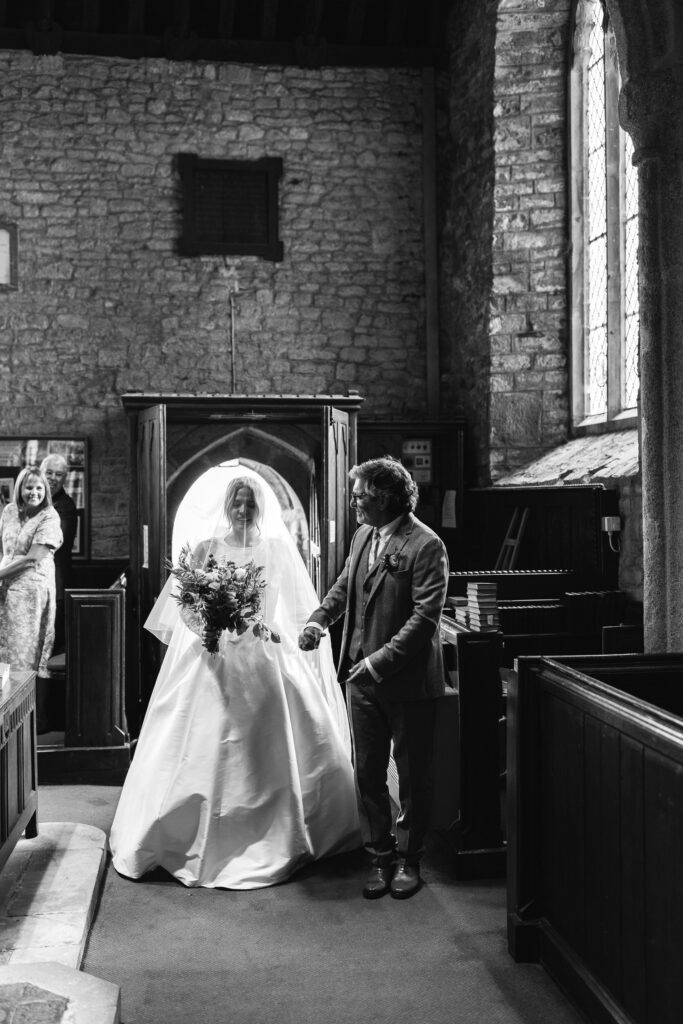 father of the bride escorts his daughter inside church black and white photography