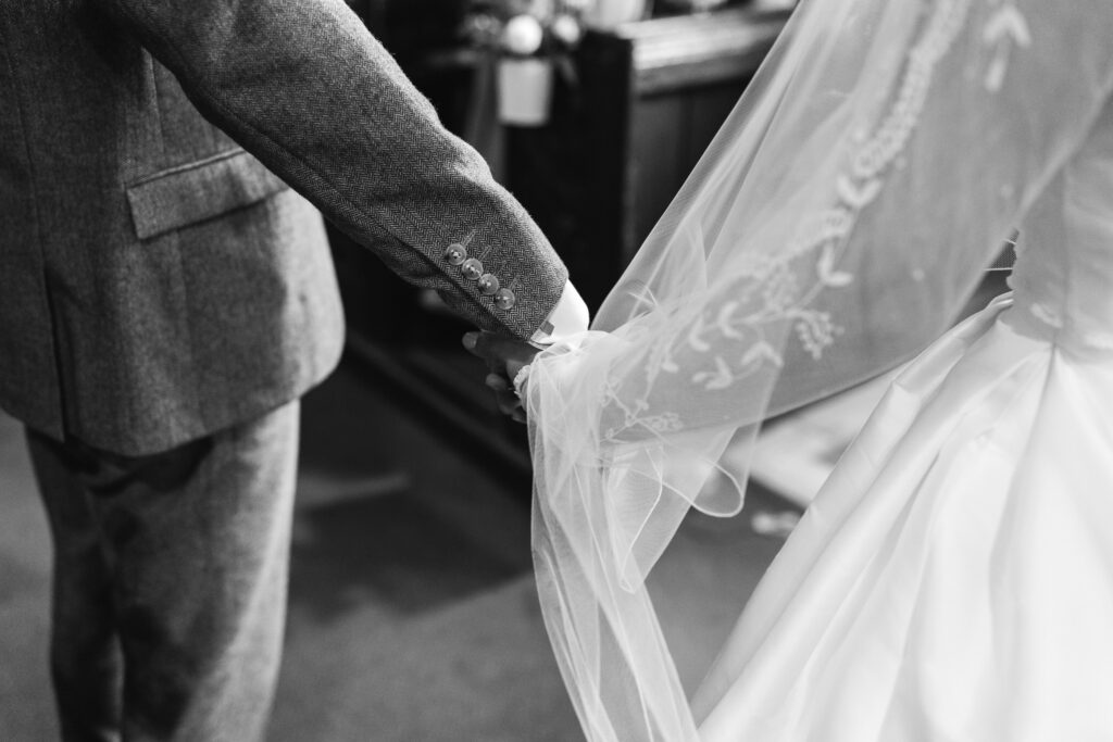 Bride holds fathers hand as he escorts her down the isle to her wedding