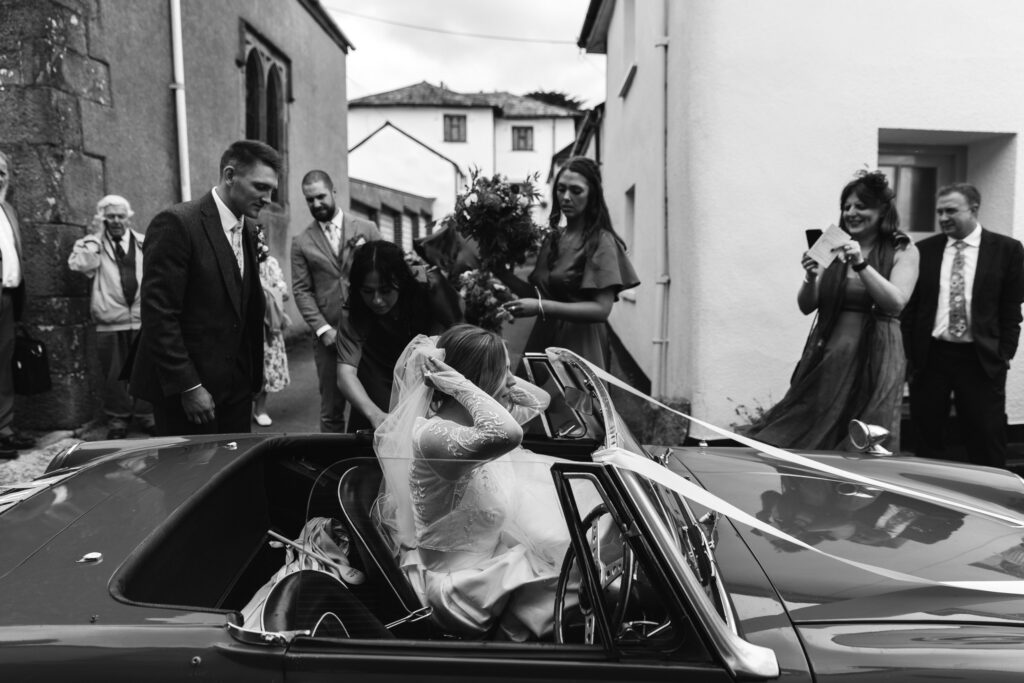 Bride leaving ceremony in wedding car during candid moment, captured in black and white photography