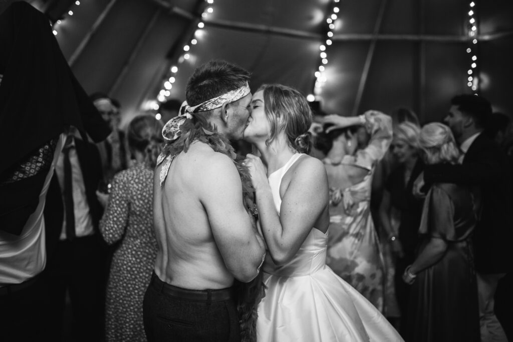 Bride and groom kissing on dancefloor during candid natural moment black and white photography and videography Rustic farm family wedding in devon