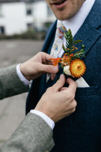 Best man putting on groom buttonhole Rustic farm family wedding in devon