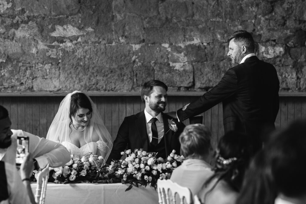 Father of the bride embraces groom in candid black and white photo