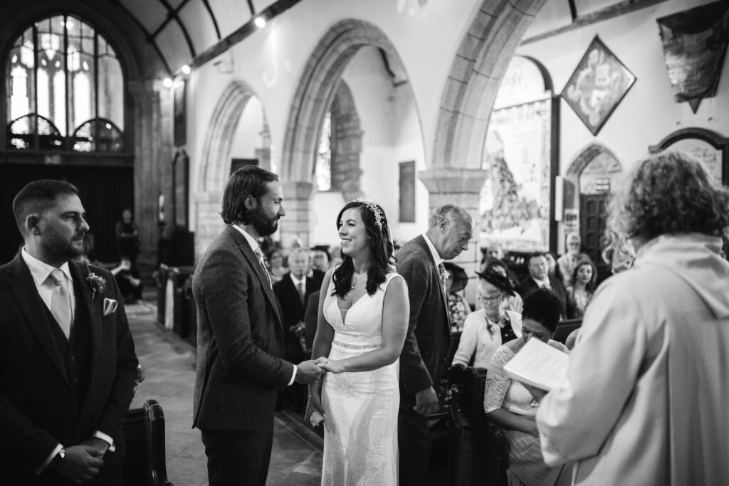 Bride and groom hold hands at the front of the church as they say their vowels on their wedding day