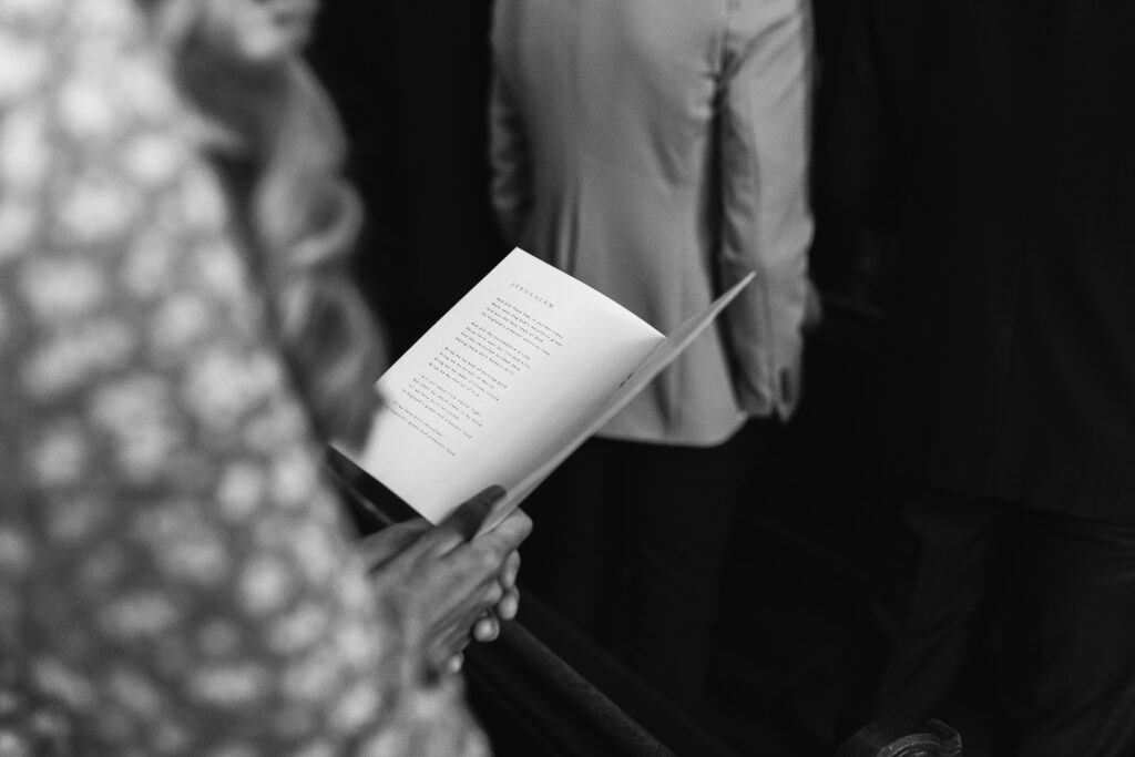 Guest holds order of service whilst singing a hymn in church on a wedding day 