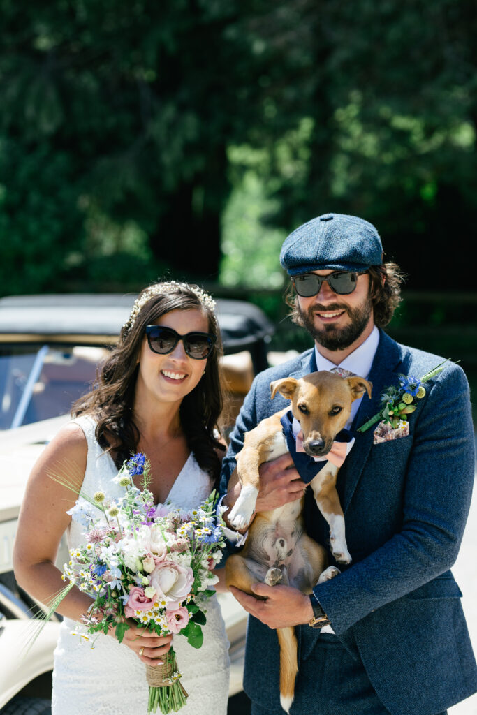 Bride and groom pose for the camera holding their pet dog 