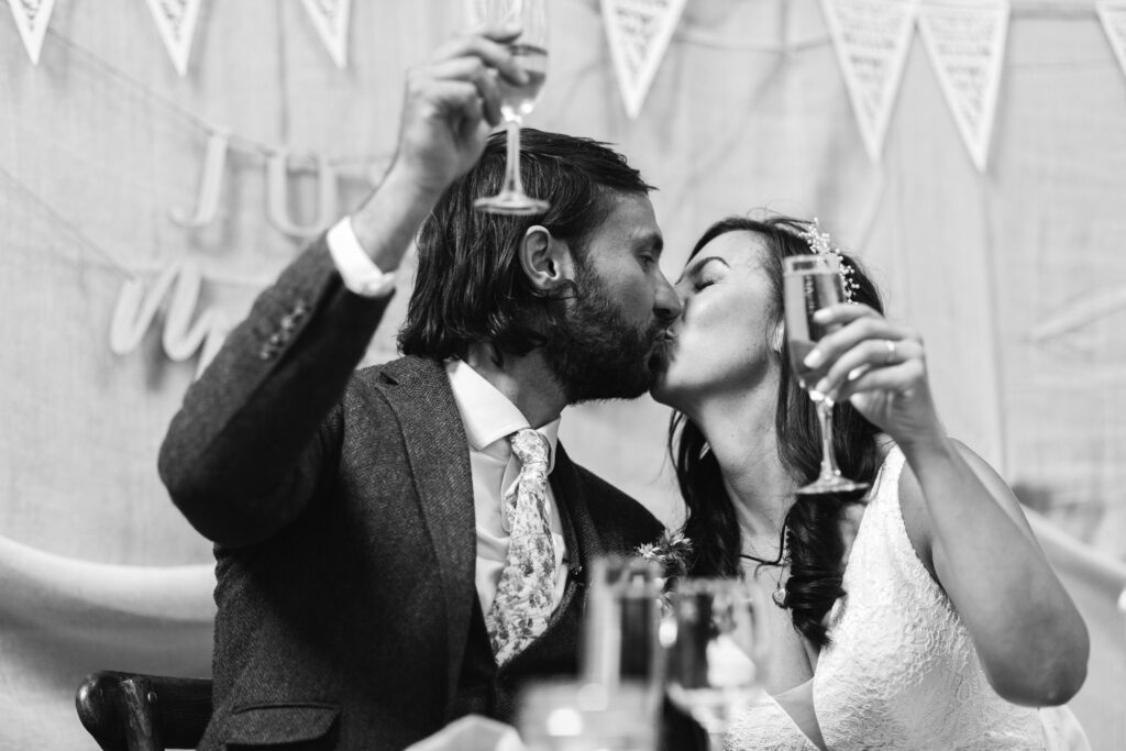 Bride and groom kiss and hold their glasses up during the toast