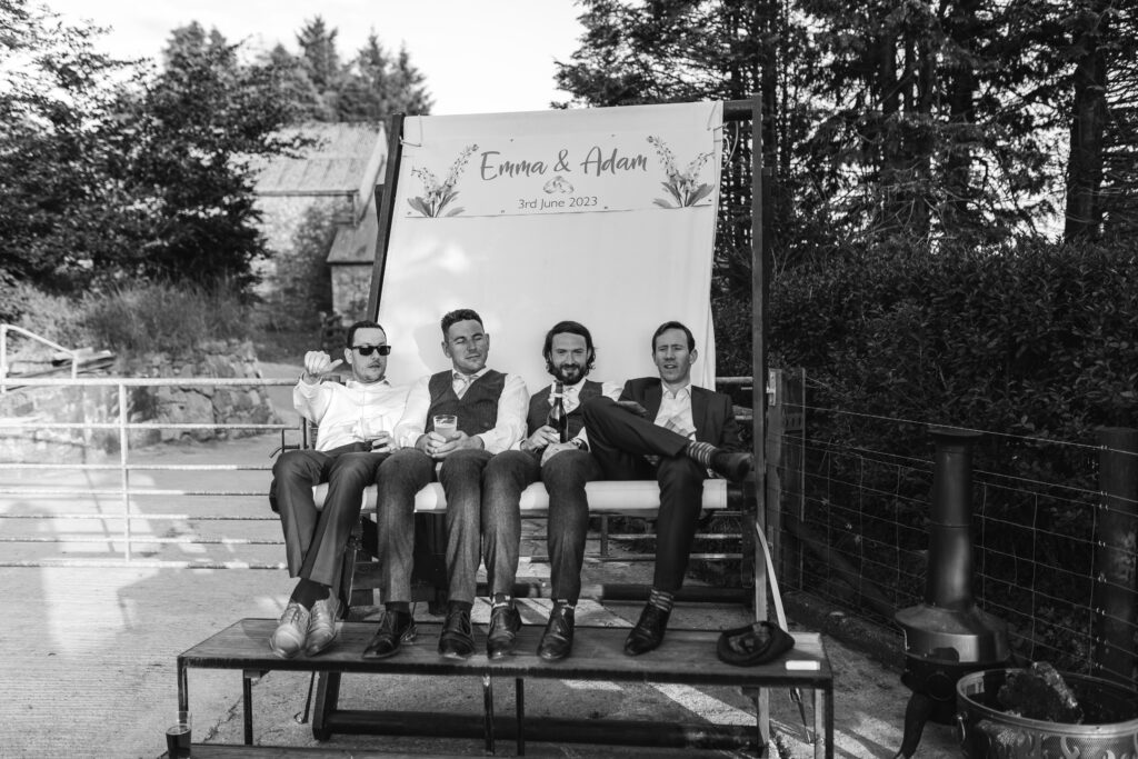 wedding guests sit on giant deckchair at reception and enjoy a drink