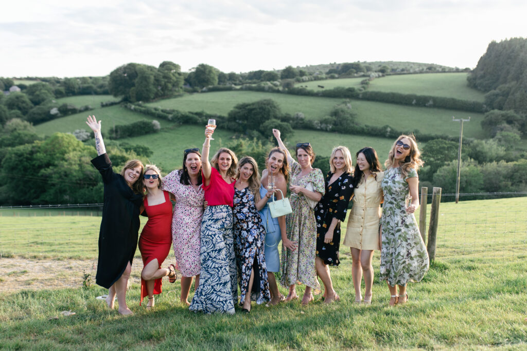 Female wedding guests smile and pose for the camera in a feild by the reception