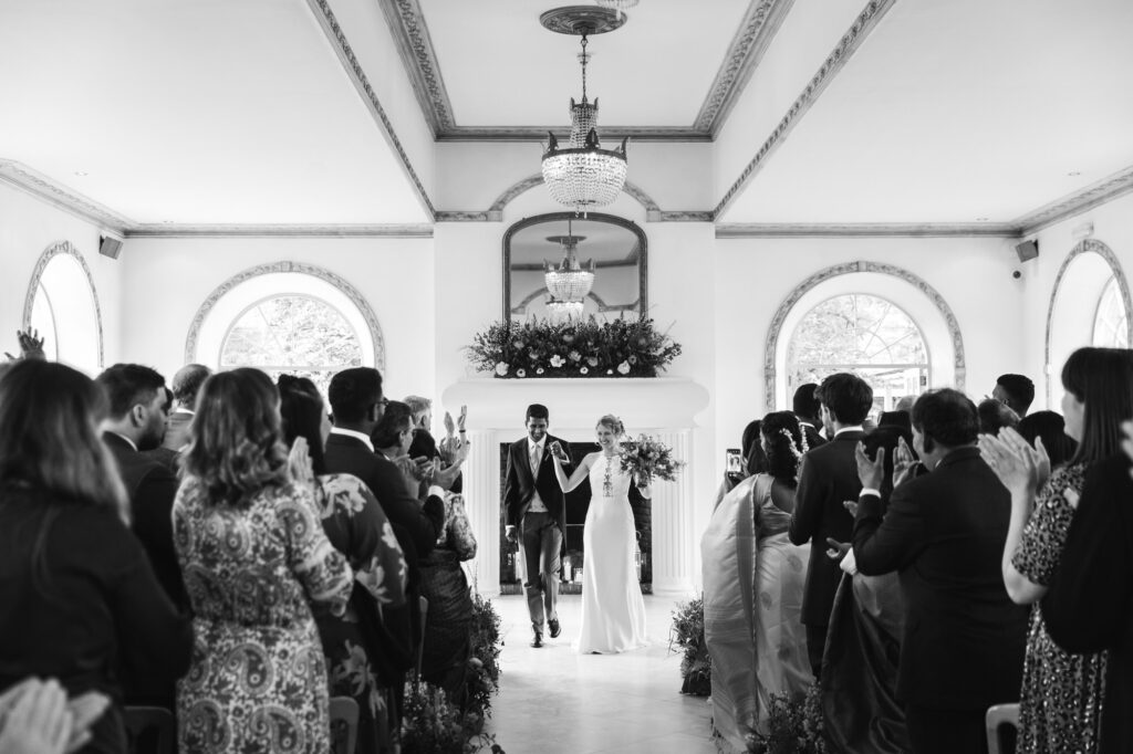 Bride and groom leave ceremony whilst guests clap 