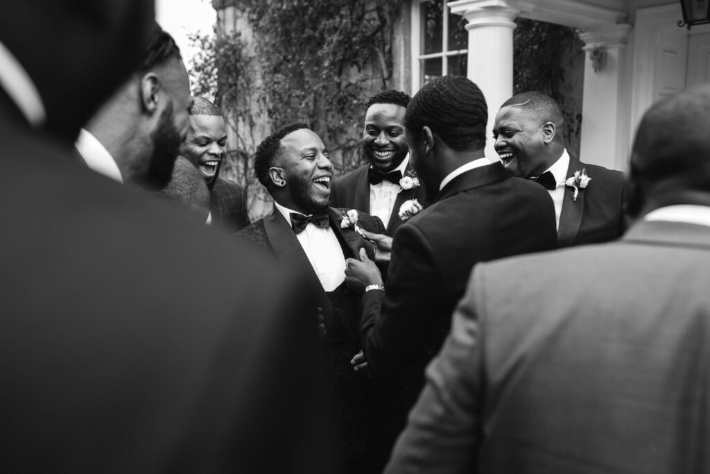 Groomsmen adjust grooms jacket and laugh during wedding day 